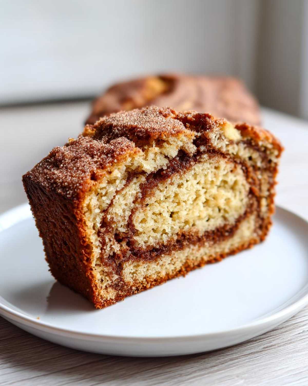 A thick slice of snickerdoodle zucchini bread featuring a prominent cinnamon swirl and sugary topping.