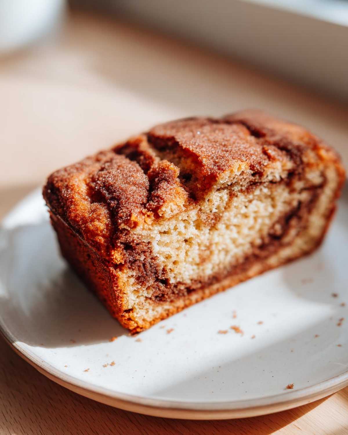 A close-up of a slice of moist snickerdoodle zucchini bread featuring a prominent cinnamon swirl and sugary topping.