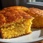 Close-up of two golden-brown slices of moist sourdough cornbread served on a white plate.