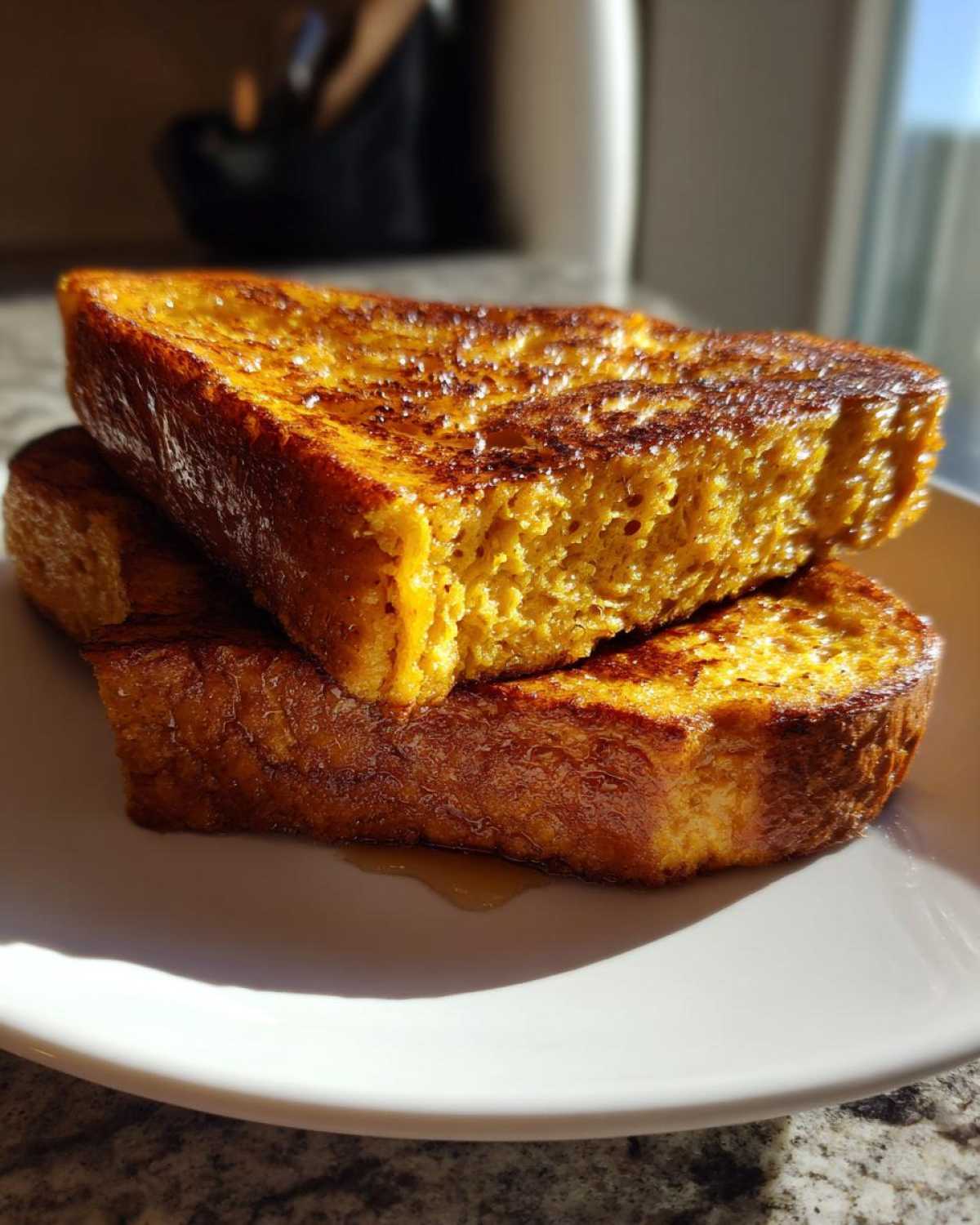 Two thick slices of golden brown sourdough french toast stacked on a white plate, glistening with syrup.