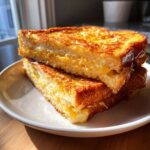A stack of thick, golden-brown sourdough french toast slices, drizzled with syrup, ready to eat.