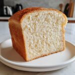 A thick slice of fluffy, white sourdough sandwich bread showing a soft, even crumb texture.