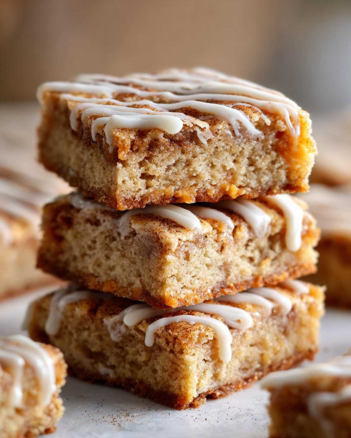 Three square snickerdoodle blondies stacked, drizzled with white vanilla icing.