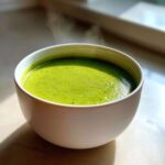 Close-up of a white bowl filled with vibrant, steaming green zucchini soup.