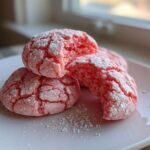 Three bright pink strawberry cake mix cookies dusted with powdered sugar on a white plate.