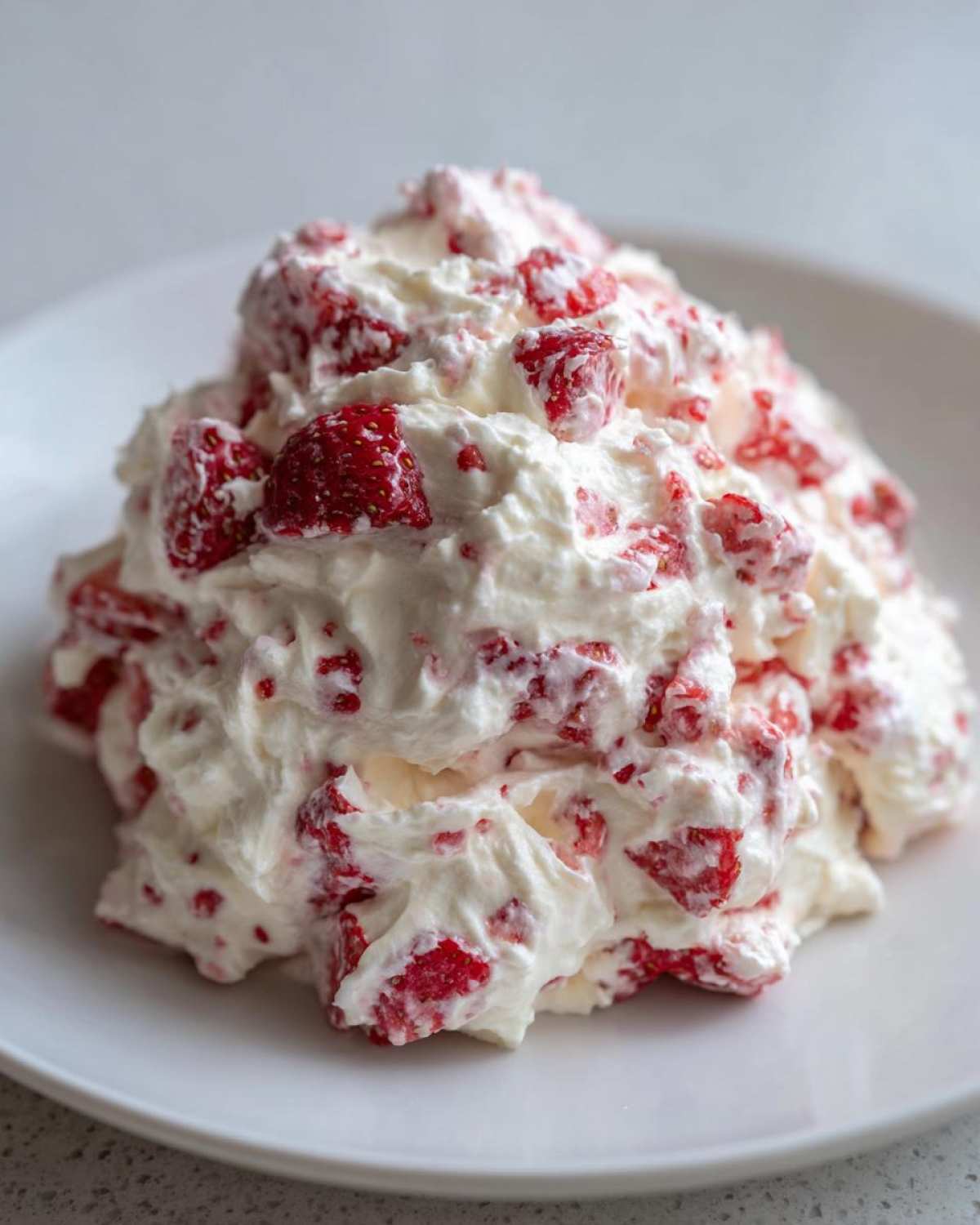 A close-up of a mound of fluffy, white strawberry cheesecake dip mixed with chunks of bright red strawberries.