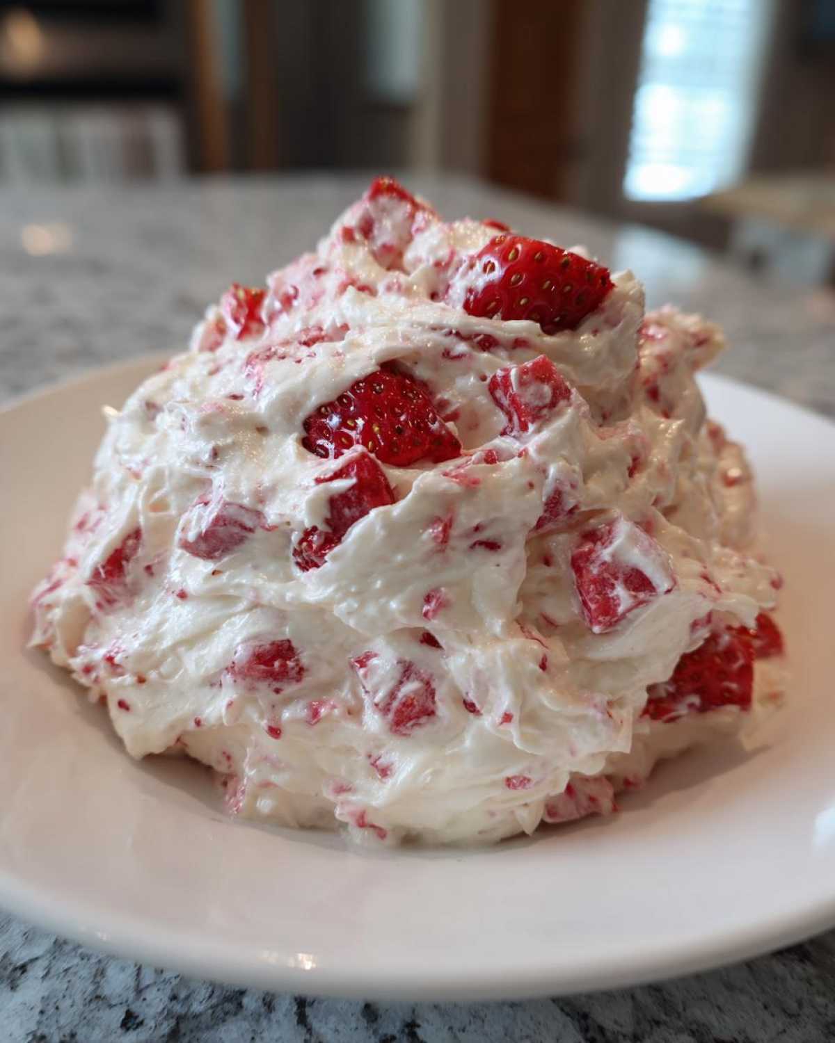 A mound of creamy, white strawberry cheesecake dip mixed with diced red strawberries, served on a white plate.