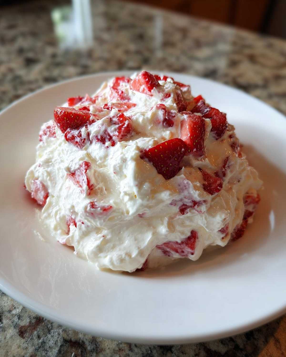 A mound of creamy white strawberry cheesecake dip mixed with chunks of fresh strawberries, served on a white plate.