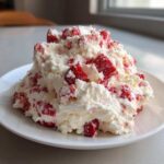 A mound of creamy, white strawberry cheesecake dip mixed with chunks of bright red strawberries, served on a white plate.