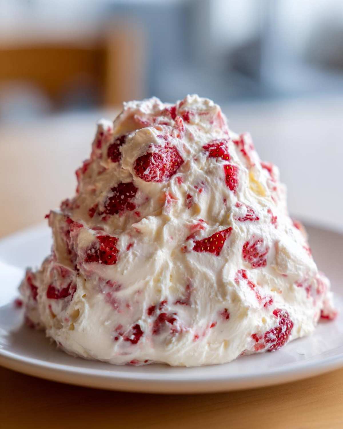 A generous mound of creamy strawberry cheesecake dip mixed with visible chunks of fresh strawberries served on a white plate.