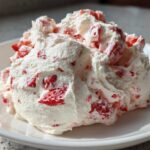 A close-up of a generous scoop of creamy strawberry cheesecake dip mixed with visible chunks of red strawberries.