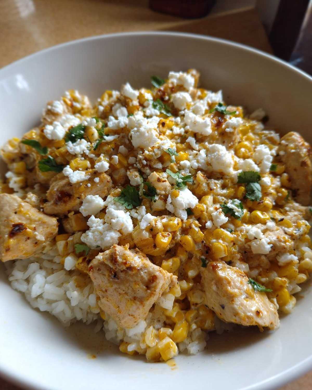 Close-up of a street corn chicken rice bowl featuring seasoned chicken chunks, creamy corn, and crumbled white cheese.