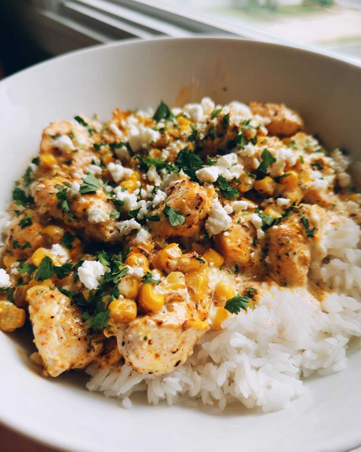 Close-up of a street corn chicken rice bowl topped with cotija cheese and cilantro.