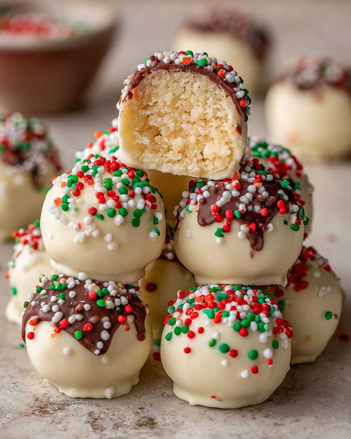 A stack of white chocolate coated sugar cookie truffles decorated with red, green, and white sprinkles.