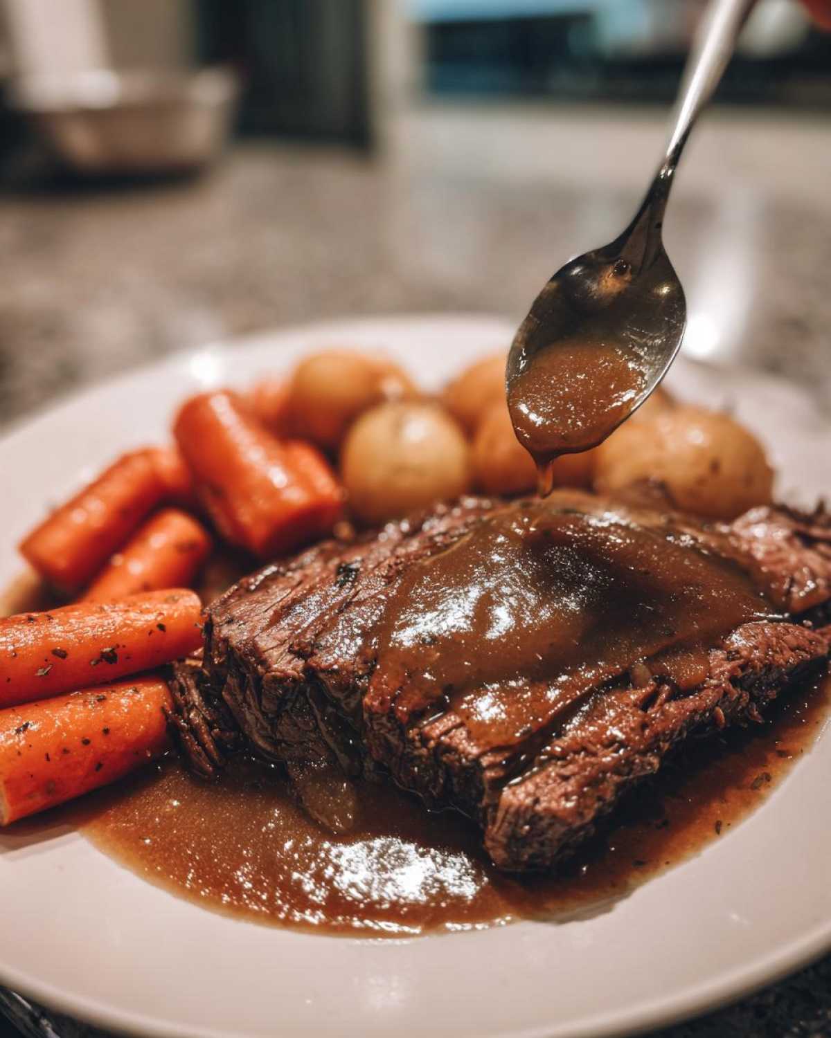 A close-up of a slice of tender pot roast covered in brown gravy, served with carrots and potatoes.