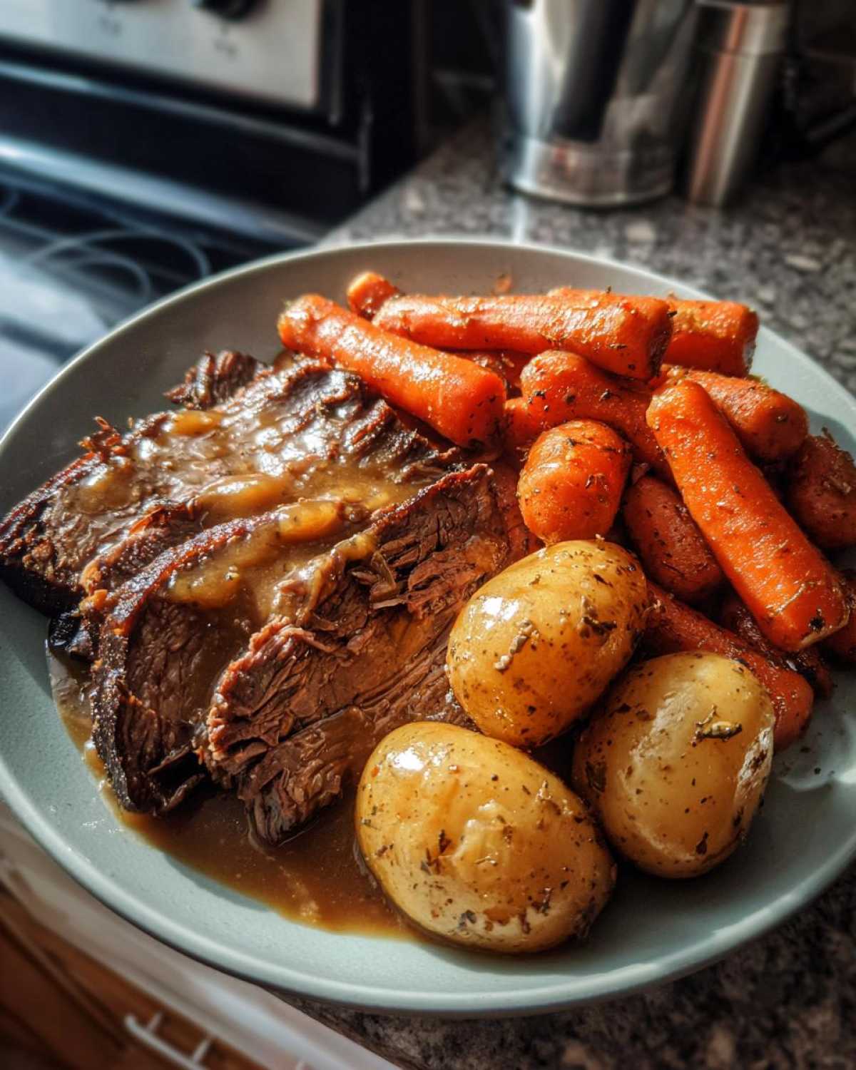 Slices of tender pot roast covered in gravy, served with roasted carrots and small seasoned potatoes.