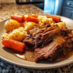 Close-up of a plate featuring tender, shredded pot roast covered in gravy, served with carrots and potatoes.