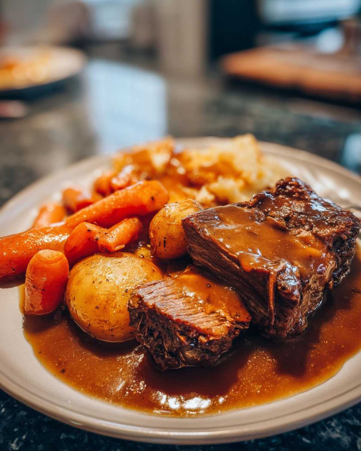 A plate featuring tender pot roast slices covered in rich brown gravy, served with roasted carrots and small potatoes.