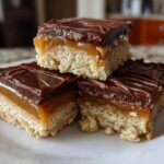 Three stacked square twix cookies bars featuring shortbread, caramel, and chocolate topping.
