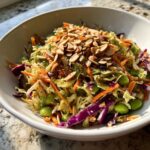 A vibrant bowl of Asian-inspired cabbage salad featuring shredded cabbage, carrots, edamame, and toasted almonds.