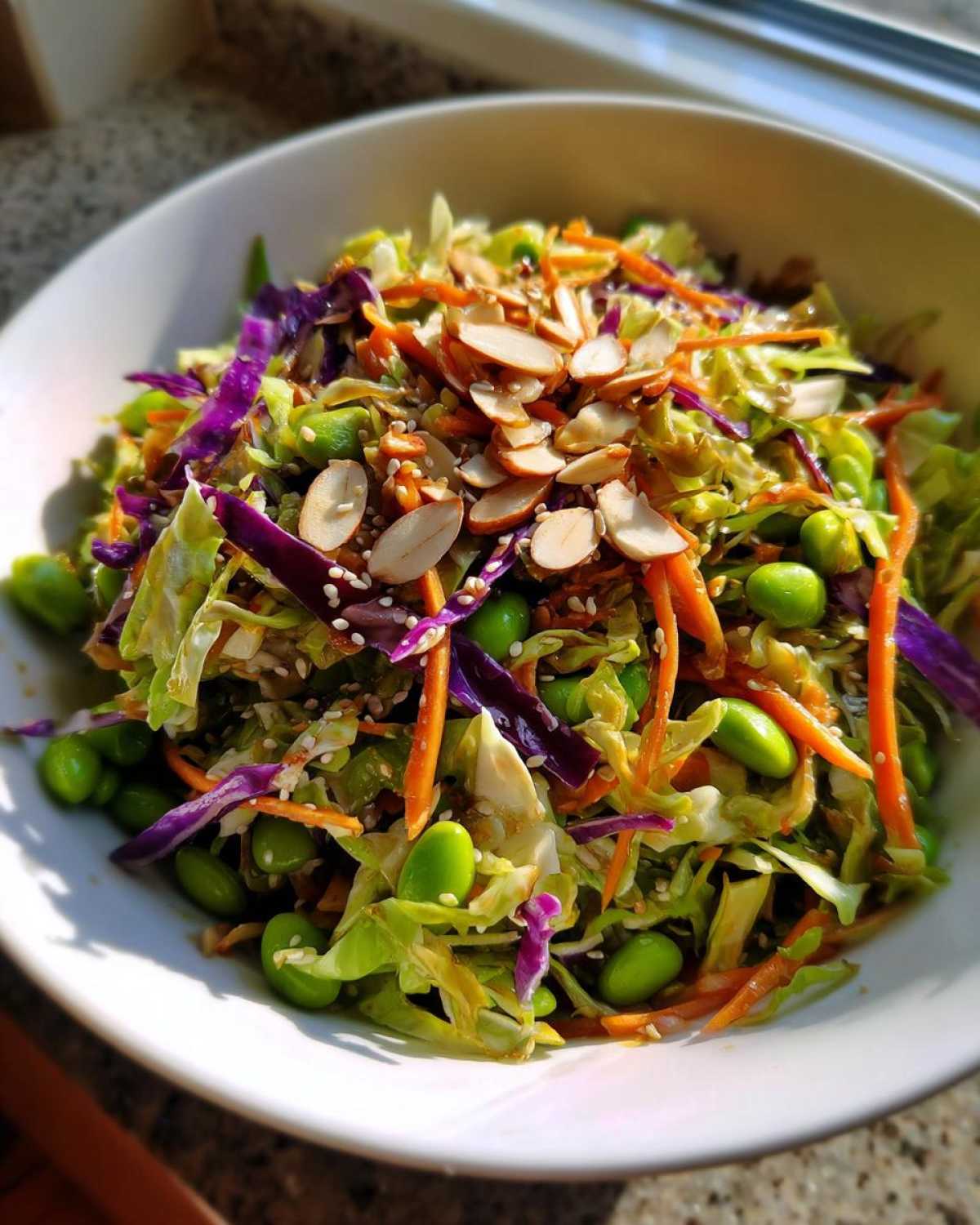 Close-up of a vibrant cabbage salad featuring shredded green cabbage, purple cabbage, carrots, edamame, and sliced almonds.