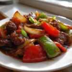 Close-up of saucy chinese pepper steak with bright red and green bell peppers and onions.