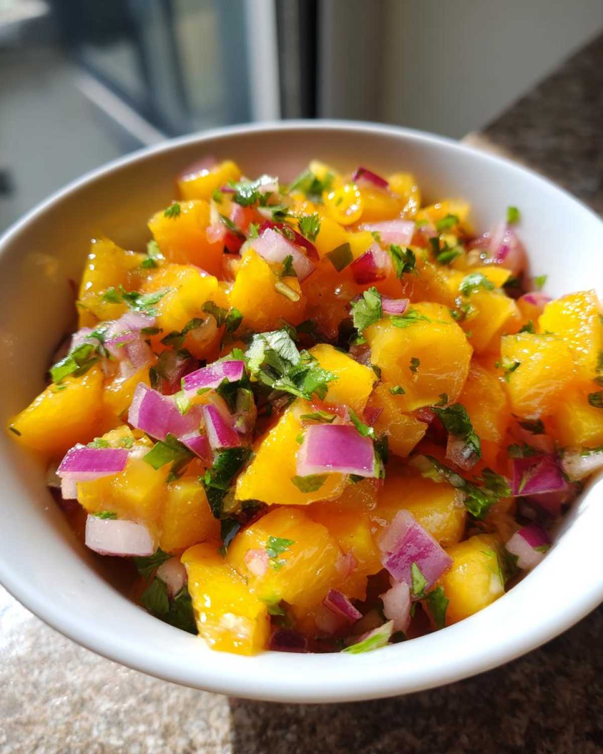 Close-up of a white bowl filled with bright orange diced peaches, red onion, and cilantro, showcasing fresh peach salsa.