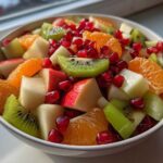 Close-up of a vibrant winter fruit salad featuring kiwi, orange segments, apple chunks, and bright pomegranate seeds.