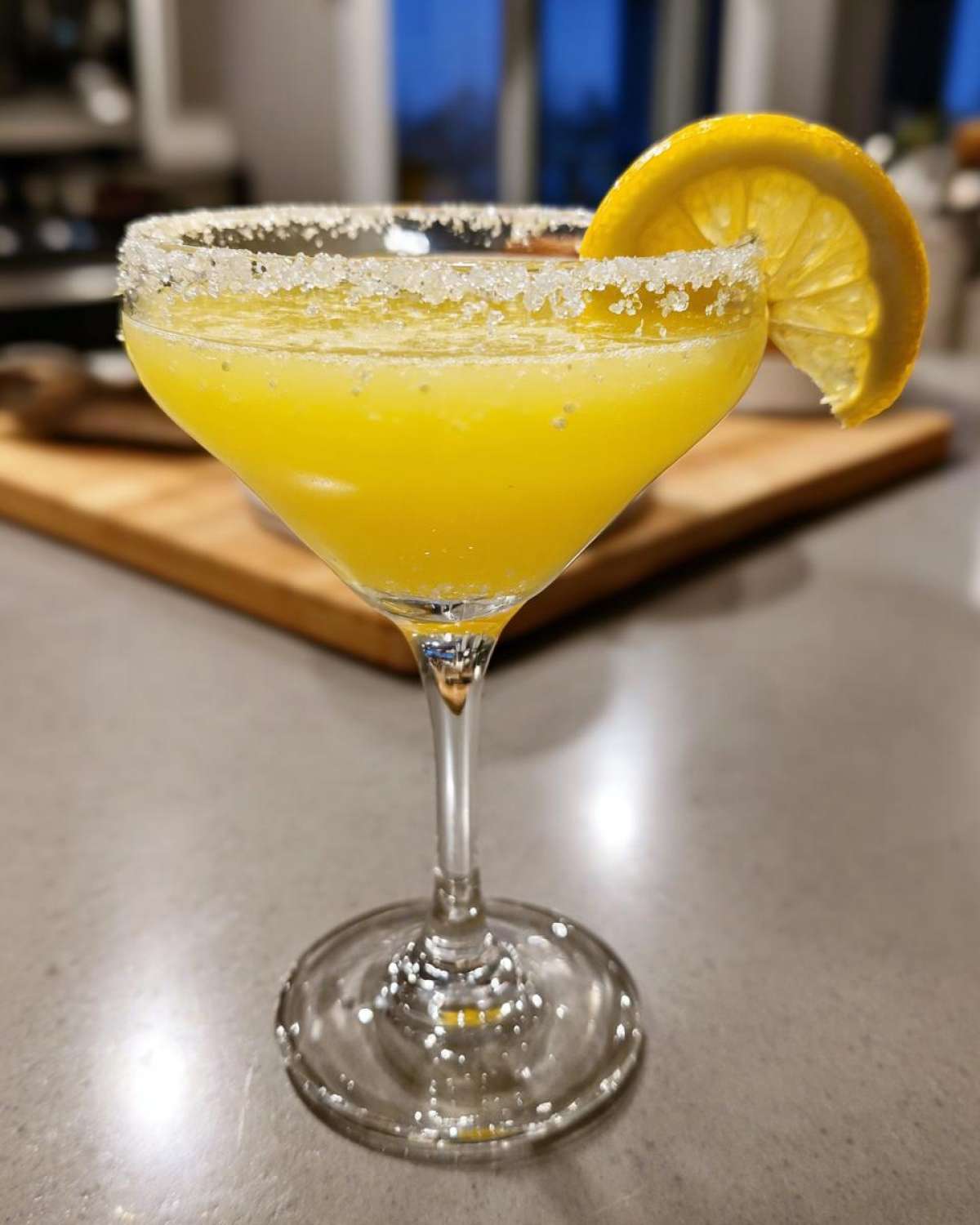 A bright yellow lemon drop cocktail in a stemmed glass with a thick sugar rim and lemon slice garnish.