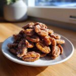 A close-up of a mound of freshly made candied pecans coated heavily in sparkling sugar, sitting on a white plate.