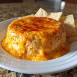A molded, warm chili cheese dip covered in melted orange cheese, served with tortilla chips on a white plate.