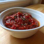 A close-up of rich, chunky homemade pizza sauce seasoned with herbs in a small white bowl.