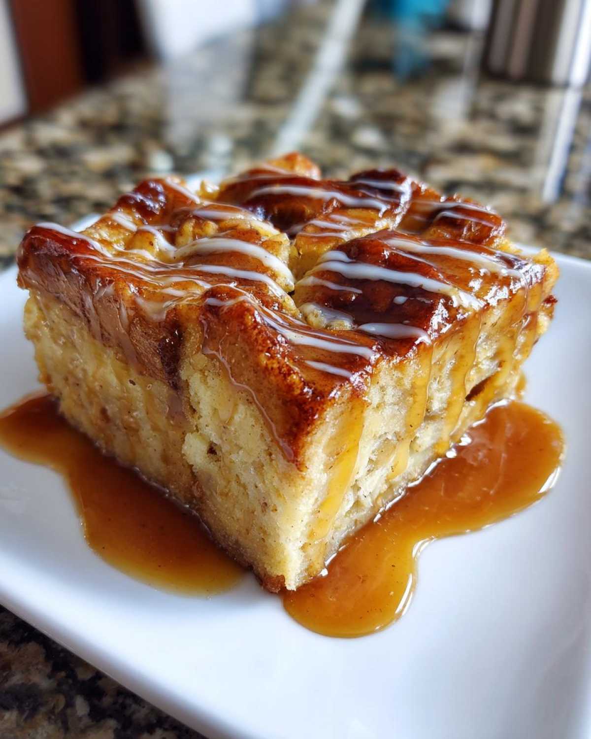 A square slice of moist apple bread pudding drizzled with caramel sauce and white icing.