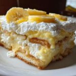 Close-up of a layered slice of amazing banana pudding topped with fresh banana slices and whipped cream.