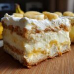 Close-up of a layered slice of amazing banana pudding featuring cream, vanilla wafers, and fresh banana slices on top.