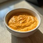Close-up of a thick, creamy, orange-colored beer cheese dip served in a small white bowl.