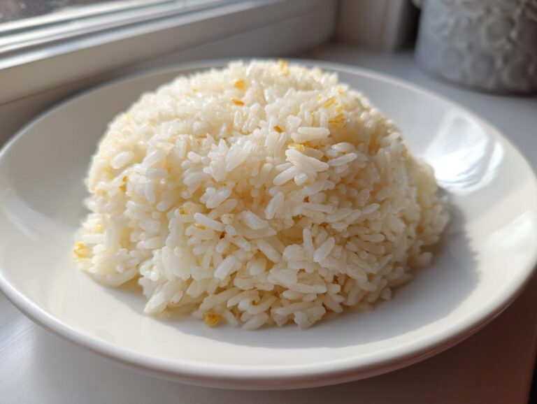 Amazing 30-Minute butter rice magic A perfectly molded mound of fluffy, white butter rice served on a bright white plate near a window.