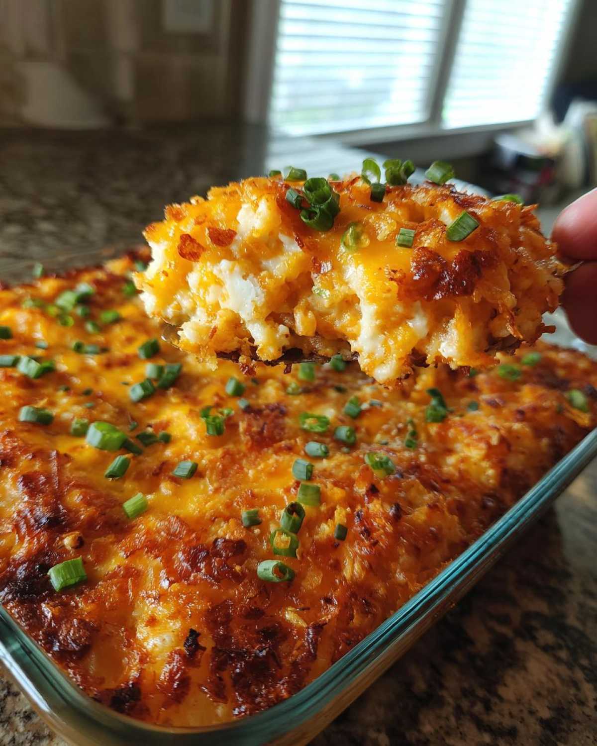 A spoonful of cheesy, baked potato casserole topped with green onions being lifted from the dish.