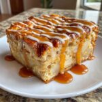 A moist slice of apple bread pudding topped with caramel and vanilla icing drizzles.