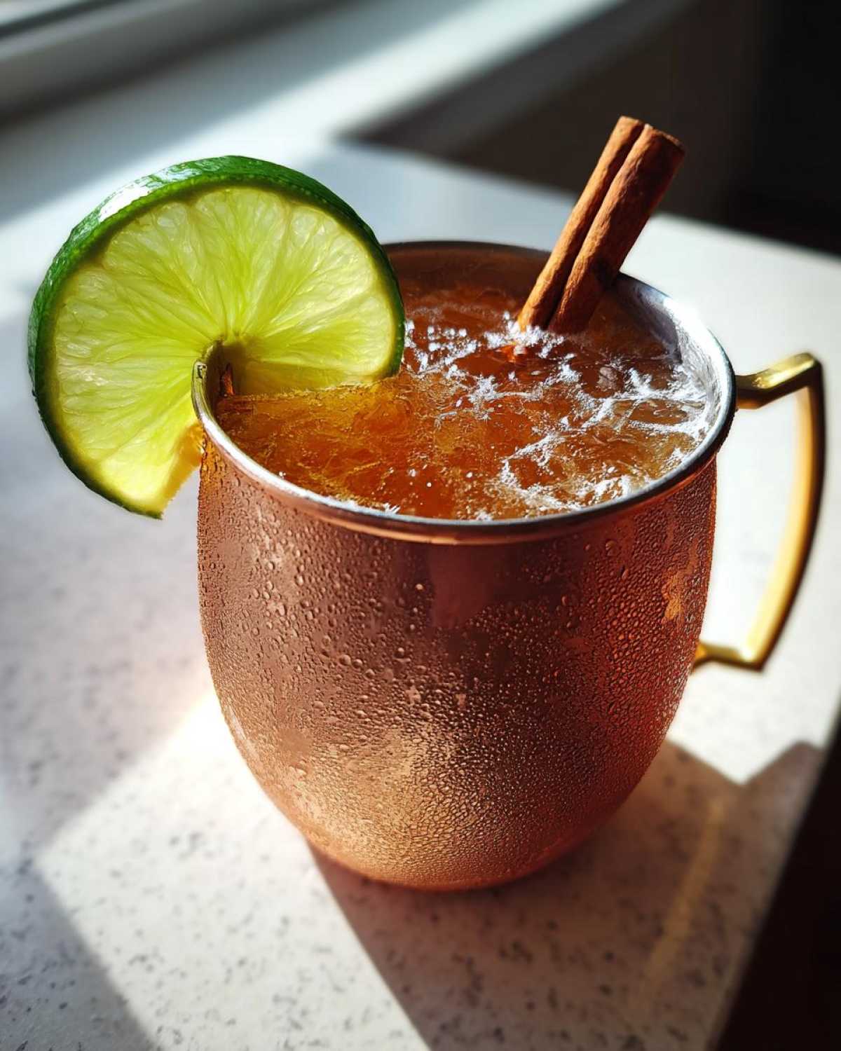 A frosty copper mug filled with an apple cider Moscow mule, garnished with a lime wheel and cinnamon sticks.