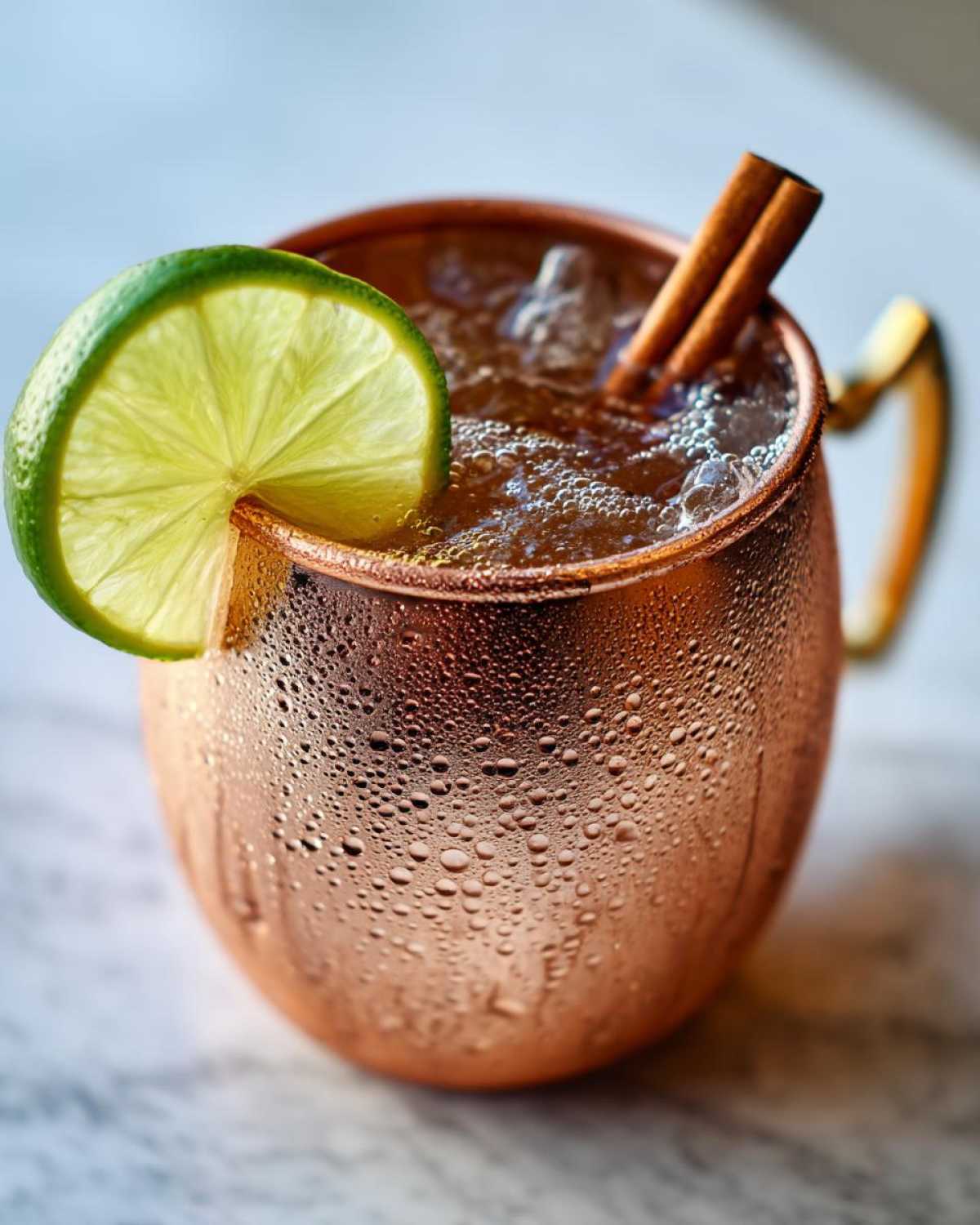 Close-up of a frosty copper mug filled with an apple cider moscow mule, garnished with lime and cinnamon sticks.