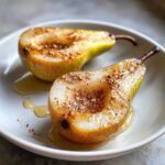 Two halves of glistening baked pears drizzled with honey and topped with nuts and spice.
