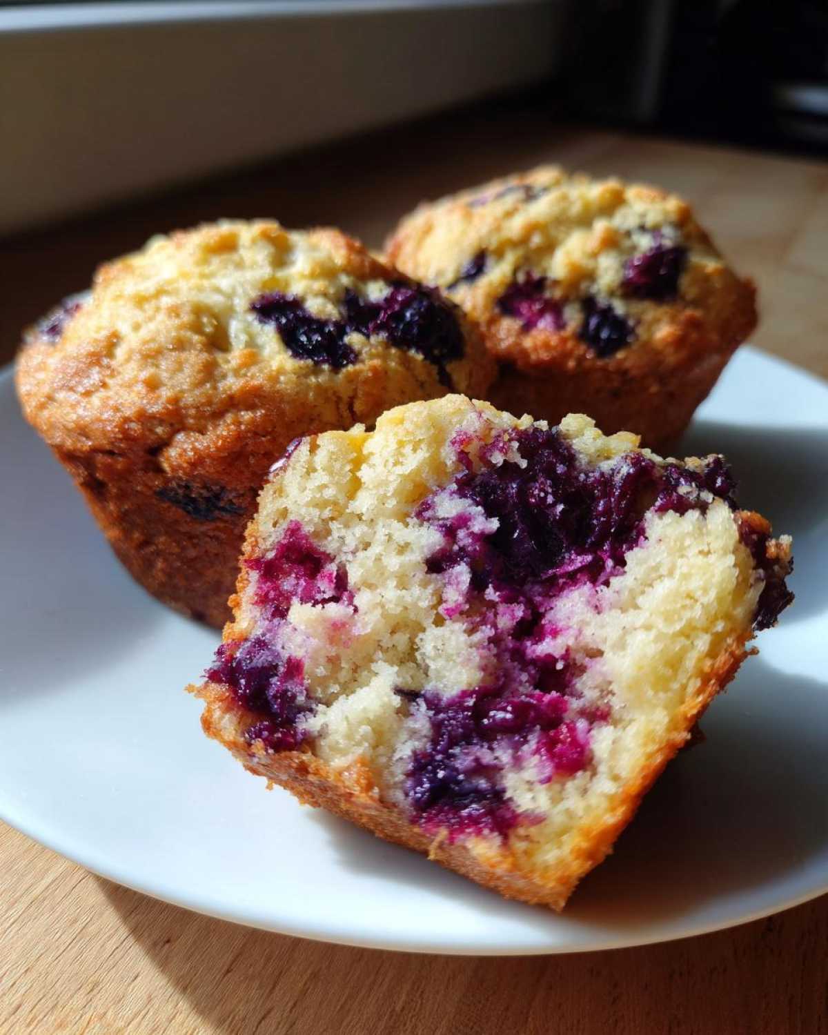 Close-up of a blueberry cottage cheese muffin cut in half showing the moist, berry-filled interior next to two whole muffins.