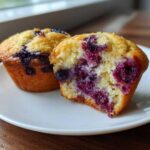 Two moist blueberry cottage cheese muffins on a white plate, one cut open showing the berry-filled interior.
