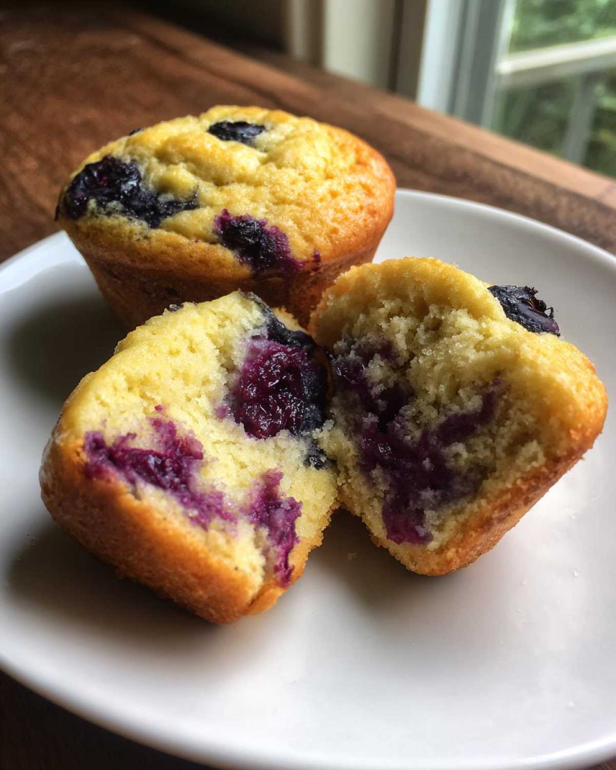 Close-up of moist blueberry cottage cheese muffins, one split open showing the purple blueberry filling.