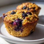 A close-up of a freshly baked blueberry oatmeal muffin with a golden, crumbly top and bursting blueberries.