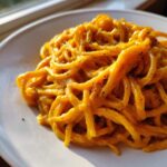 Close-up of spaghetti coated in a vibrant orange butternut squash pasta sauce, topped with cracked black pepper.