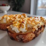 Two slices of cheesy egg toast on a white plate, featuring fluffy white egg mixture topped with melted, browned cheddar cheese.