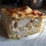 A thick, hearty slice of chicken alfredo lasagna featuring layers of pasta, creamy sauce, and chunks of white chicken meat.