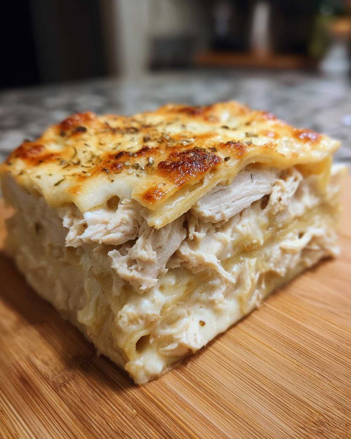 A thick, square slice of chicken alfredo lasagna showing layers of shredded chicken and creamy sauce, topped with melted, browned cheese.